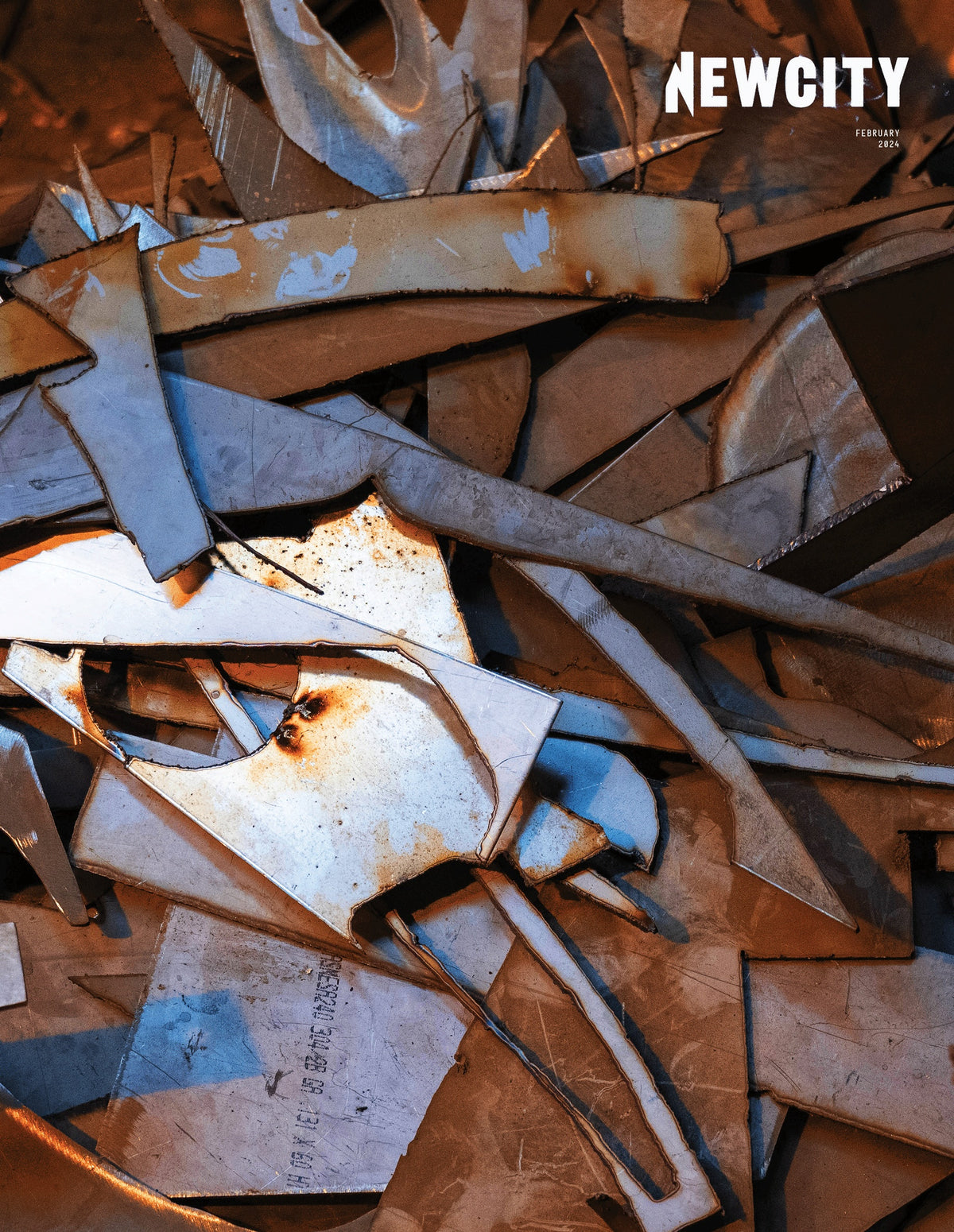 A pile of variously shaped metal and cardboard scraps in blue and brown hues, reminiscent of abstract forms found in Kansas City art, with “February 2024 Issue: 38th Anniversary Issue (Print Edition)” displayed in white text in the top right corner.