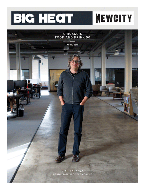 A man with glasses and gray hair stands in a modern open office space. The cover of the April 2019 Issue: Big Heat Food & Drink 50 features headlines such as BIG HEAT, NEWCITY, and Nick Kokonas: Restaurateur of the Moment, celebrating his leadership among the behind-the-kitchen players shaping Chicago’s dining scene.