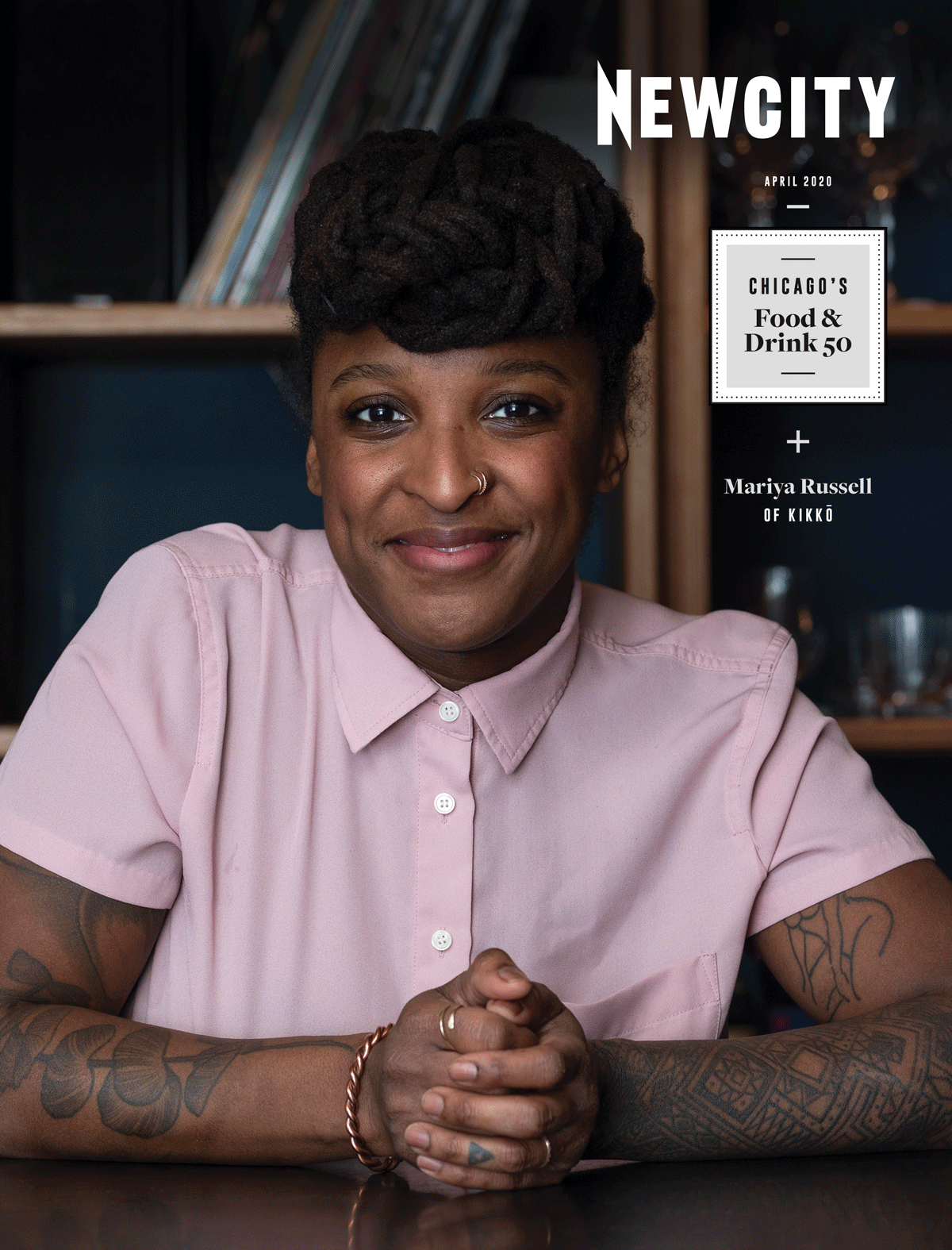 A person with styled hair, wearing a light pink shirt, sits at a table smiling. The magazine cover reads NEWCITY April 2020 Issue: Big Heat Food & Drink 50, featuring Chicago food creativity and Mariya Russell of Kikko in the Chicago's Food & Drink 50.